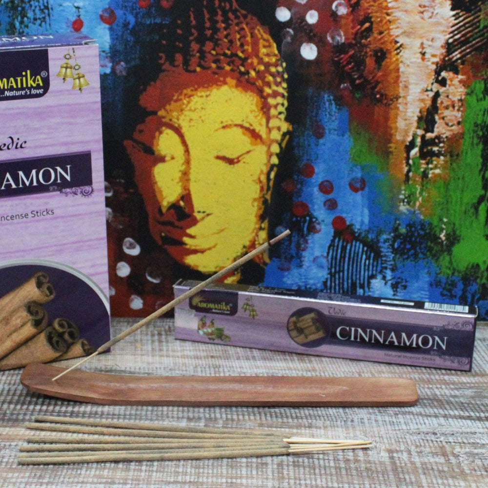 Aromatiika Cinnamon incense sticks with packaging and a wooden incense holder in front of a Buddha painting.