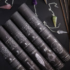 Set of black tubes with decorative labels on a dark surface with a necklace and crystal.