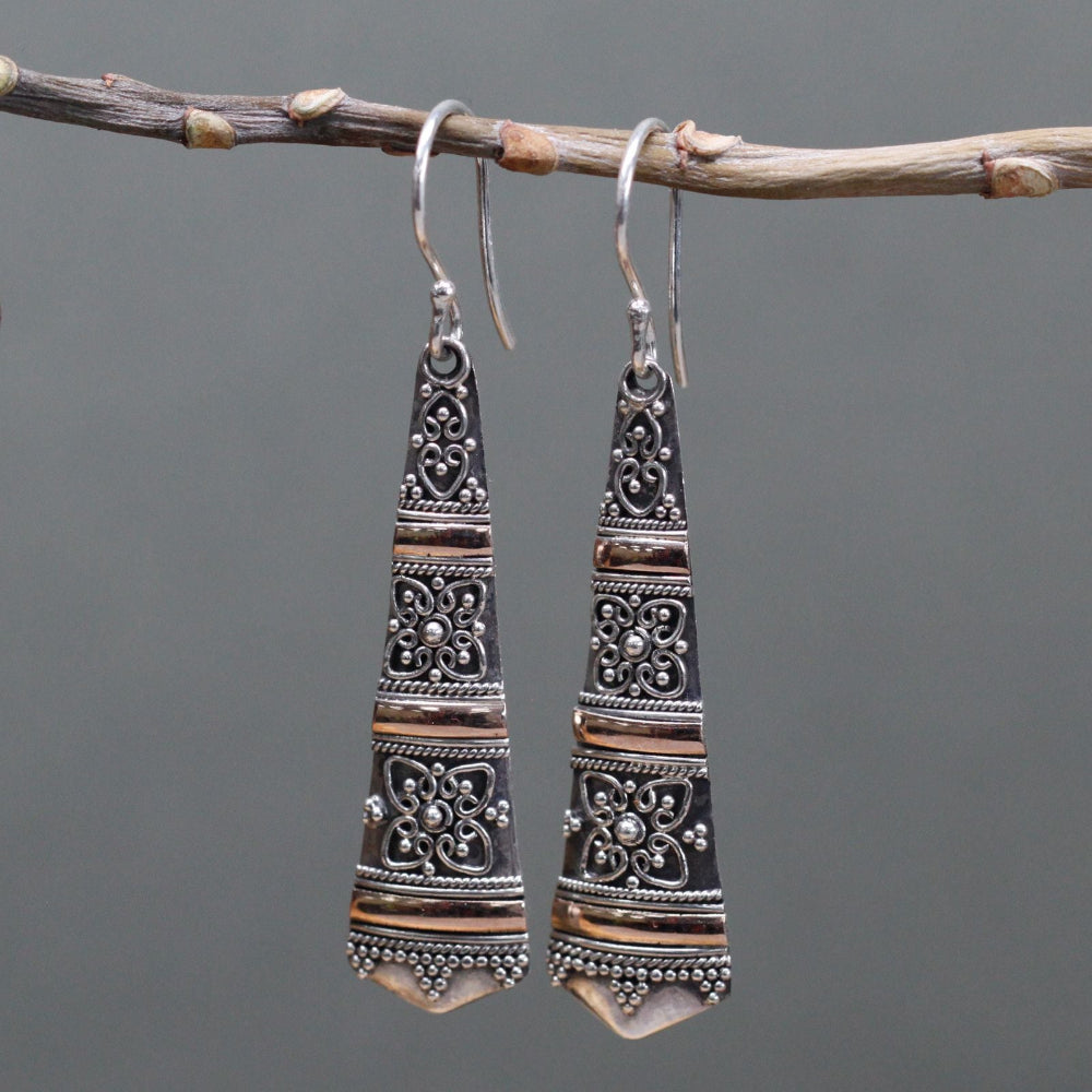 Pair of silver earrings hanging from a branch against a gray background