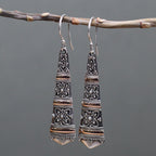 Pair of silver earrings hanging from a branch against a gray background