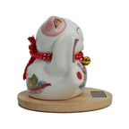 White ceramic cat figurine with colorful decorations on a wooden base against a white background