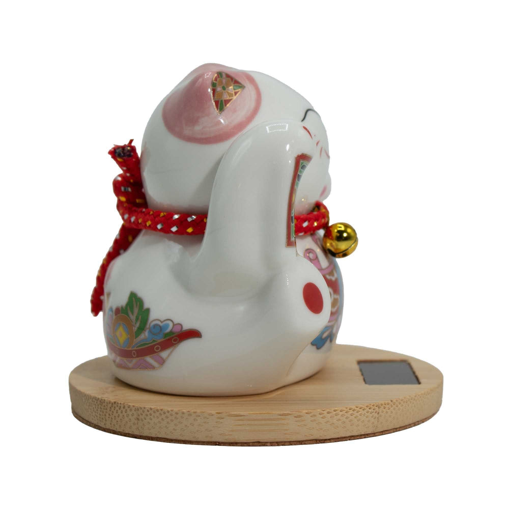 White ceramic cat figurine with colorful decorations on a wooden base against a white background