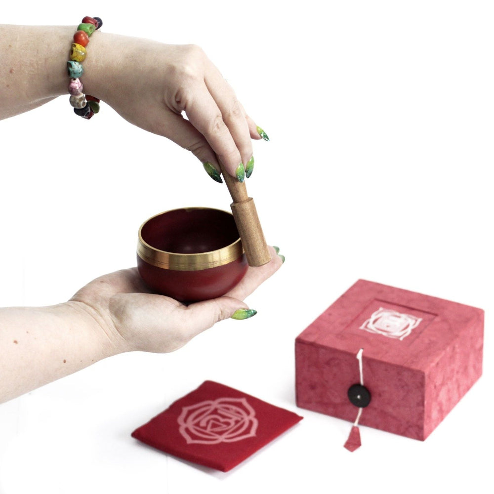 Red singing bowl with gold rim held by a hand, next to a matching red box on a white background.