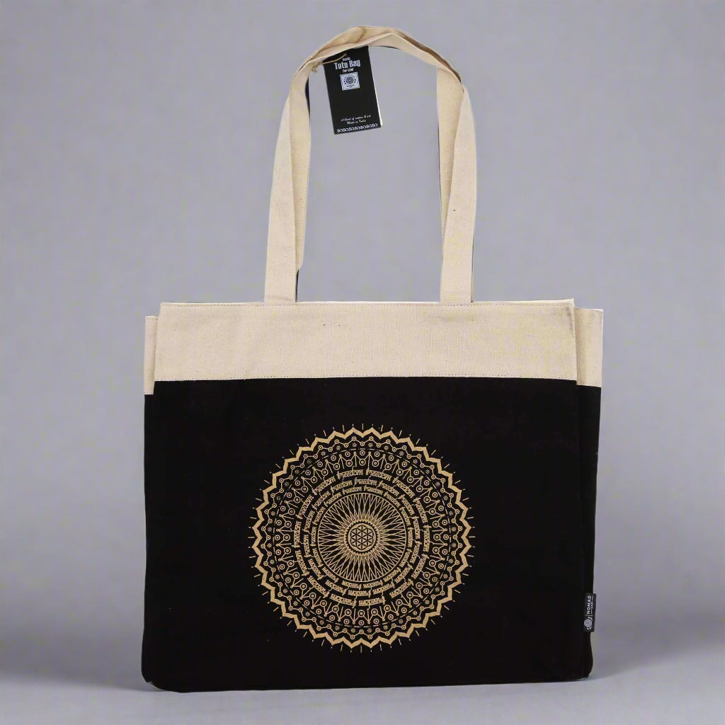Tote bag with black bottom half and beige top half, featuring a mandala design. Eleanoras