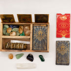 Wooden box with stones and wands, tarot cards, and a red book on a white background
