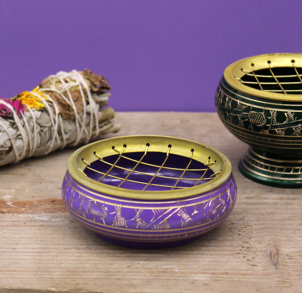 Decorative purple and gold incense burner on a wooden surface with a purple background