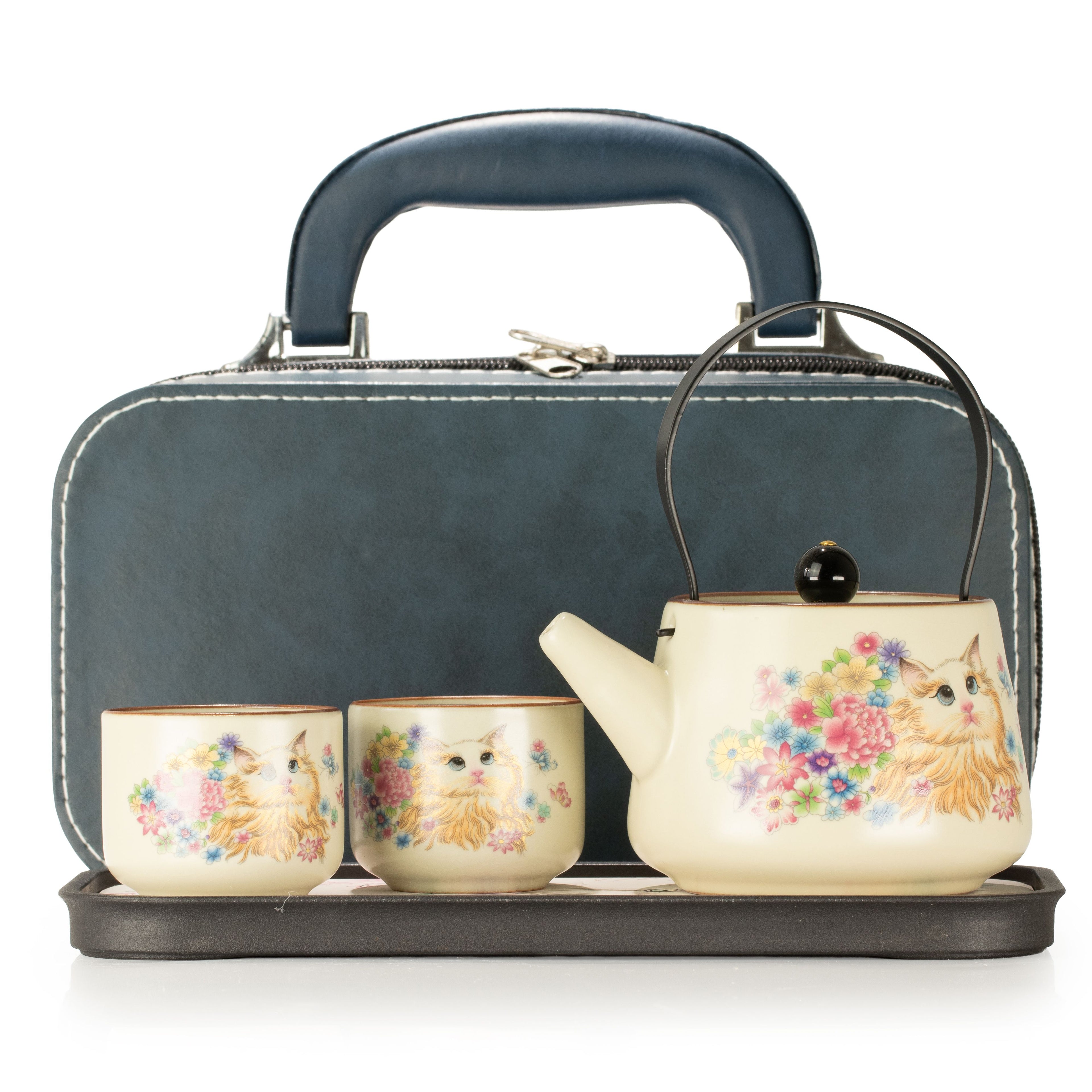 A tea set with a teapot, two cups, and a matching carrying case. The teapot and cups are cream-colored with a floral print featuring a cat, while the carrying case is dark blue-gray with a handle and zippered closure.