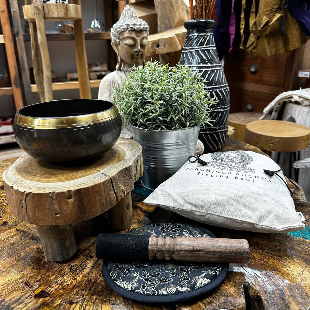 Meditation items including a singing bowl, Buddha statue, and potted plant on a wooden surface.
