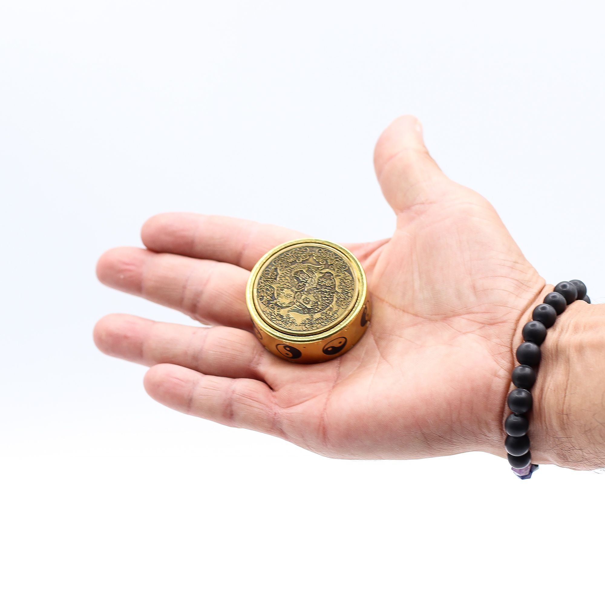 Hand holding a small round metallic object with intricate design on a white background
