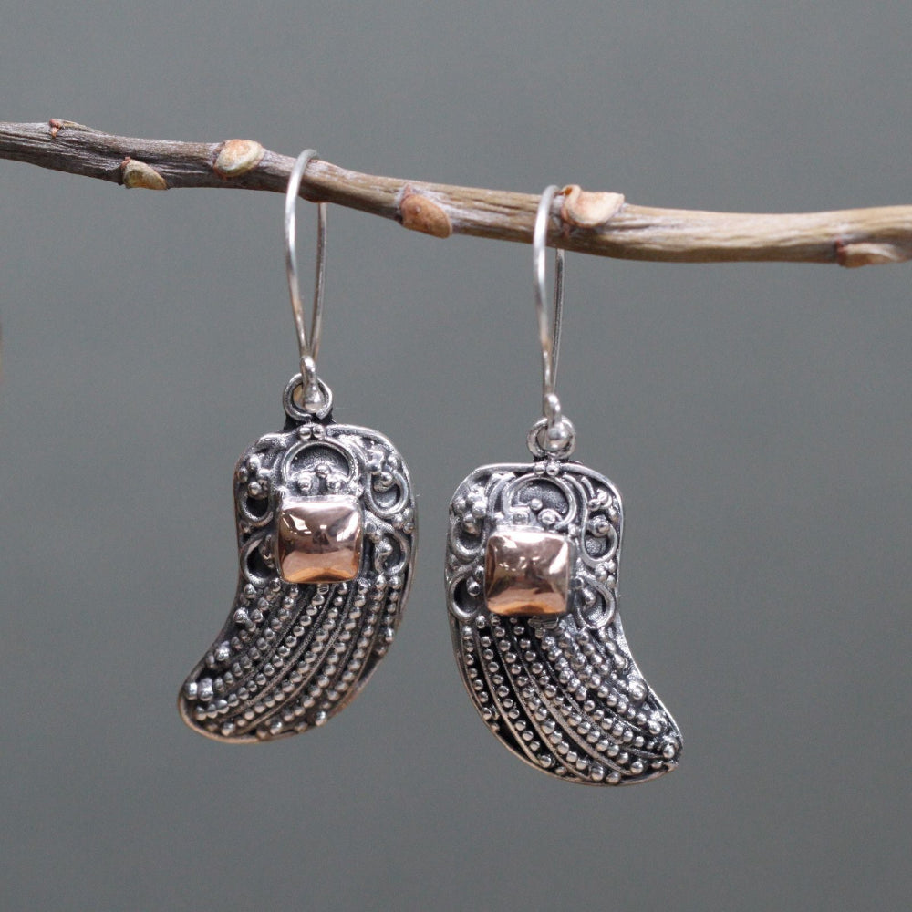 Silver boot-shaped earrings hanging on a branch against a gray background