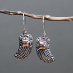 Silver boot-shaped earrings hanging on a branch against a gray background
