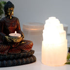 Buddha statue holding a candle next to a selenite lamp.