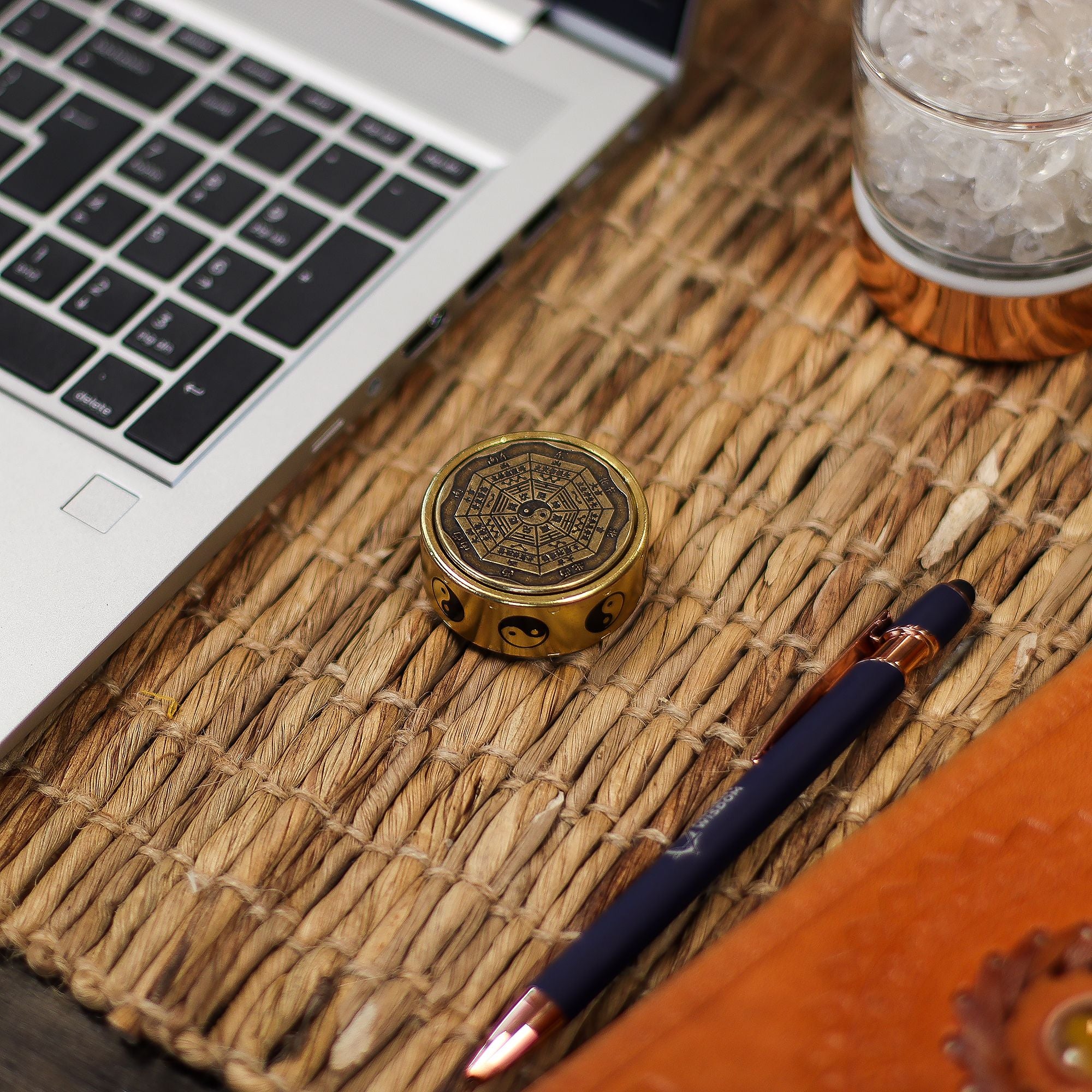 Laptop on a woven mat with a decorative metal object and pen
