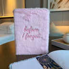 Pink fluffy notebook with 'before I forget...' text on a wooden surface.