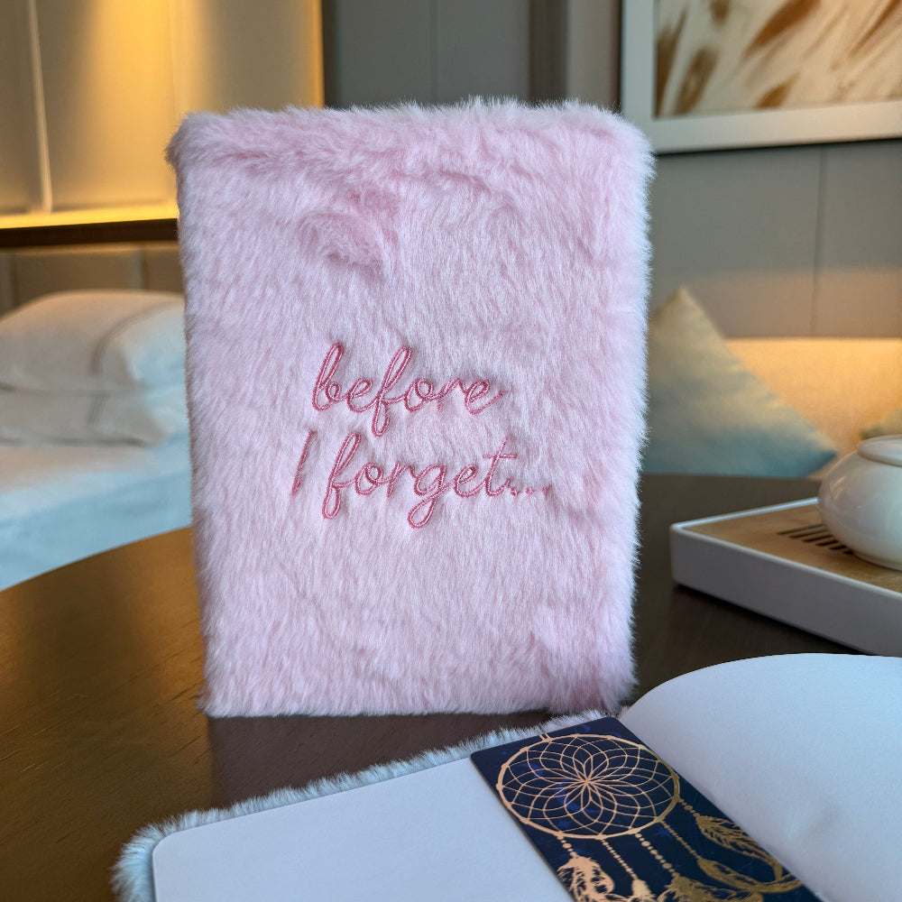 Pink fluffy notebook with 'before I forget...' text on a wooden surface.