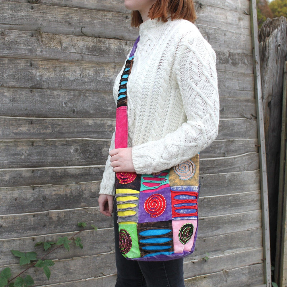 Person wearing a white cable knit sweater with a colorful skirt against a wooden fence.