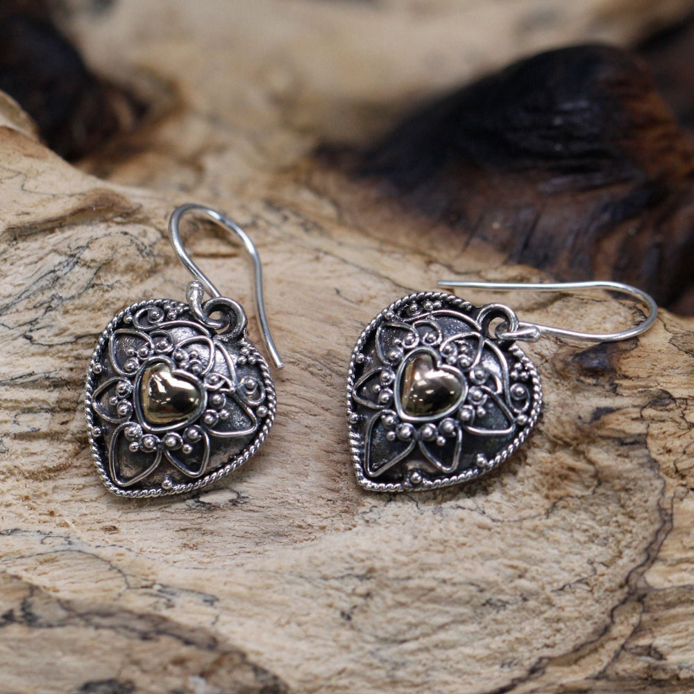 Pair of silver heart-shaped earrings with gold accents on a wooden surface