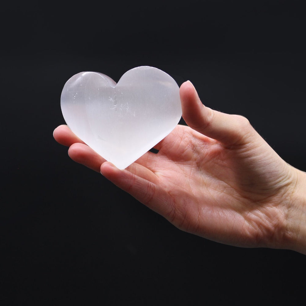 Hand holding a clear heart-shaped crystal against a black background