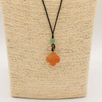 Necklace with an orange pendant and green bead on a woven beige background