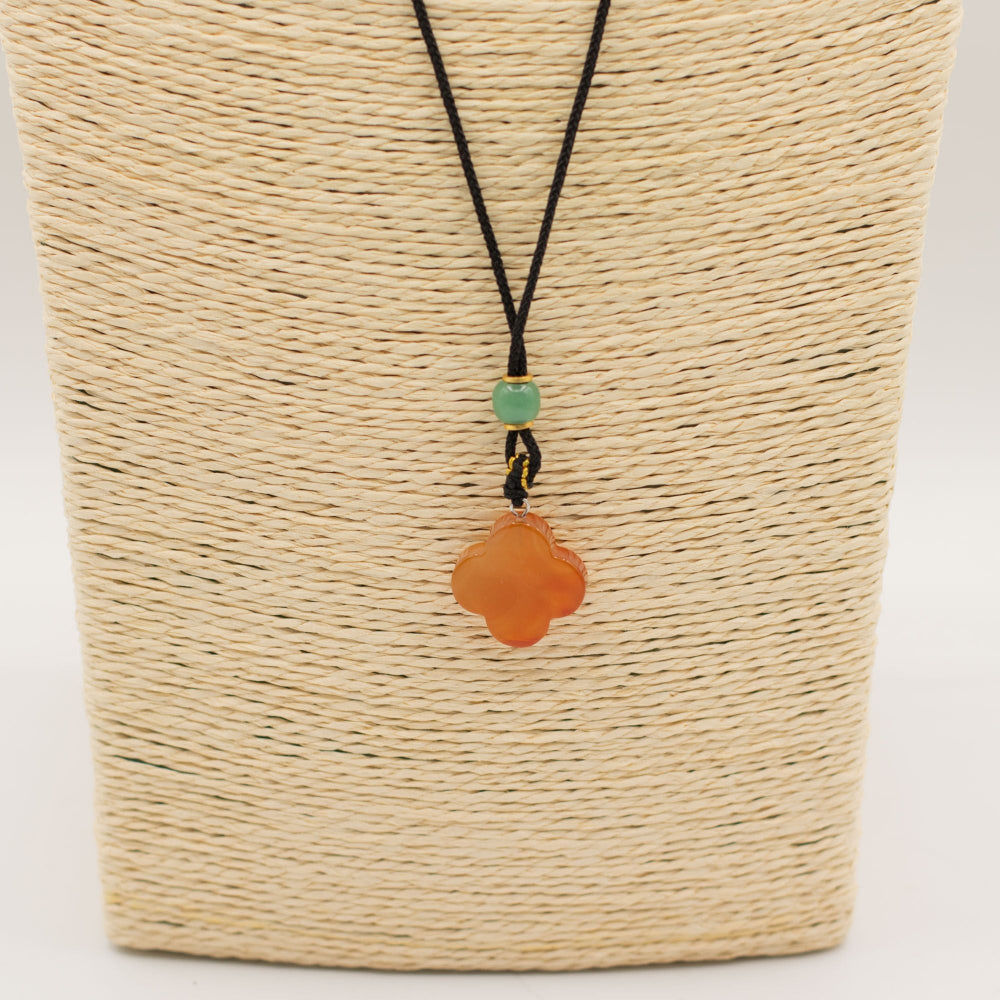 Necklace with an orange pendant and green bead on a woven beige background