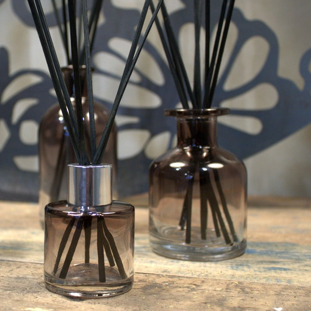 Three diffuser bottles with black sticks on a wooden surface.