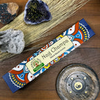 Nag Champa incense packaging on a wooden surface with crystals and a decorative plate.