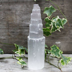 Tall, clear crystal tower with green leaves on a wooden surface