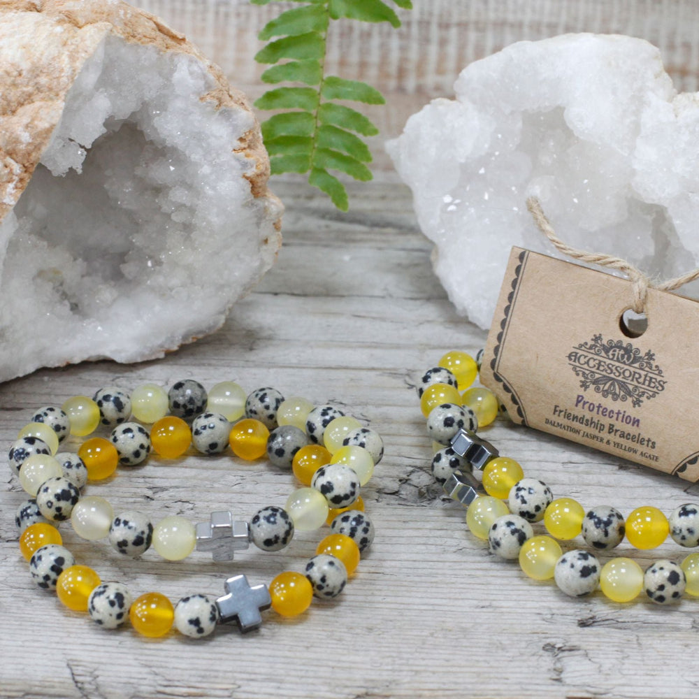 Two beaded bracelets with a tag on a wooden surface with decorative stones and plants.