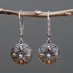 Silver earrings with intricate designs hanging on a branch against a gray background