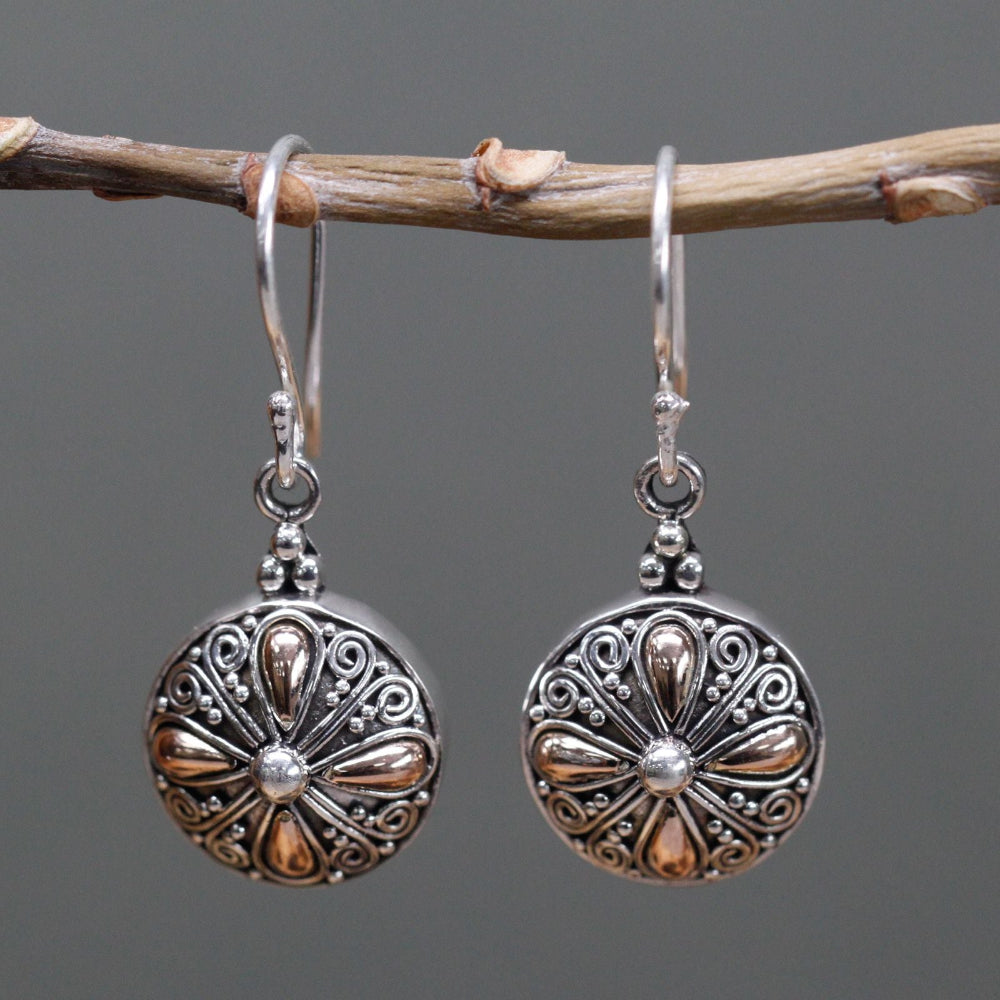 Silver earrings with intricate designs hanging on a branch against a gray background