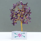 Decorative tree made of purple stones on a white base with floral design against a gray background