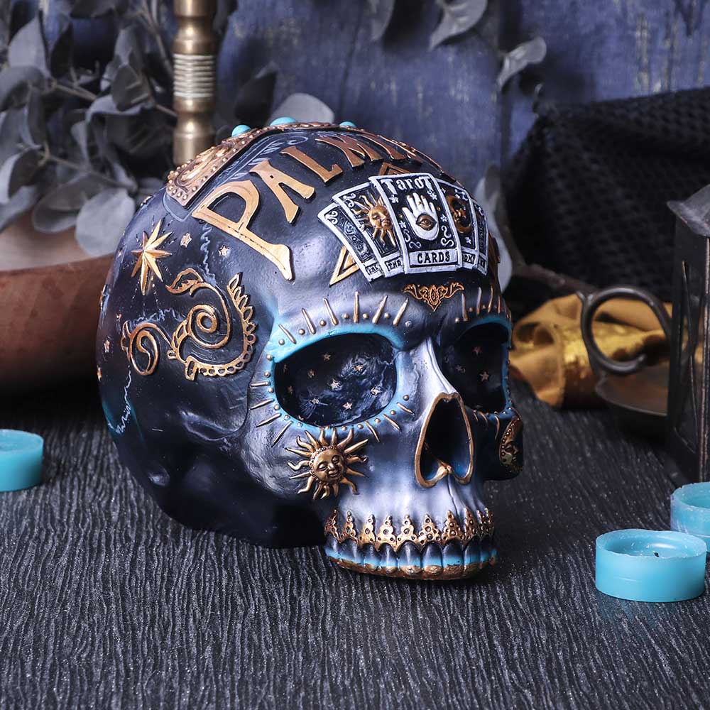 Decorative skull with palmistry design on a textured surface with candles and plants.