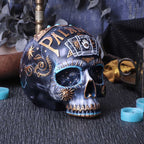 Decorative skull with palmistry design on a textured surface with candles and plants.
