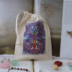 A beige drawstring pouch featuring a colorful chakra tree graphic, displayed on an open book with crystals and a pendant nearby.