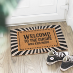 Doormat with 'Welcome to the Circus, Wild Kids Inside' text on a wooden floor with shoes nearby.