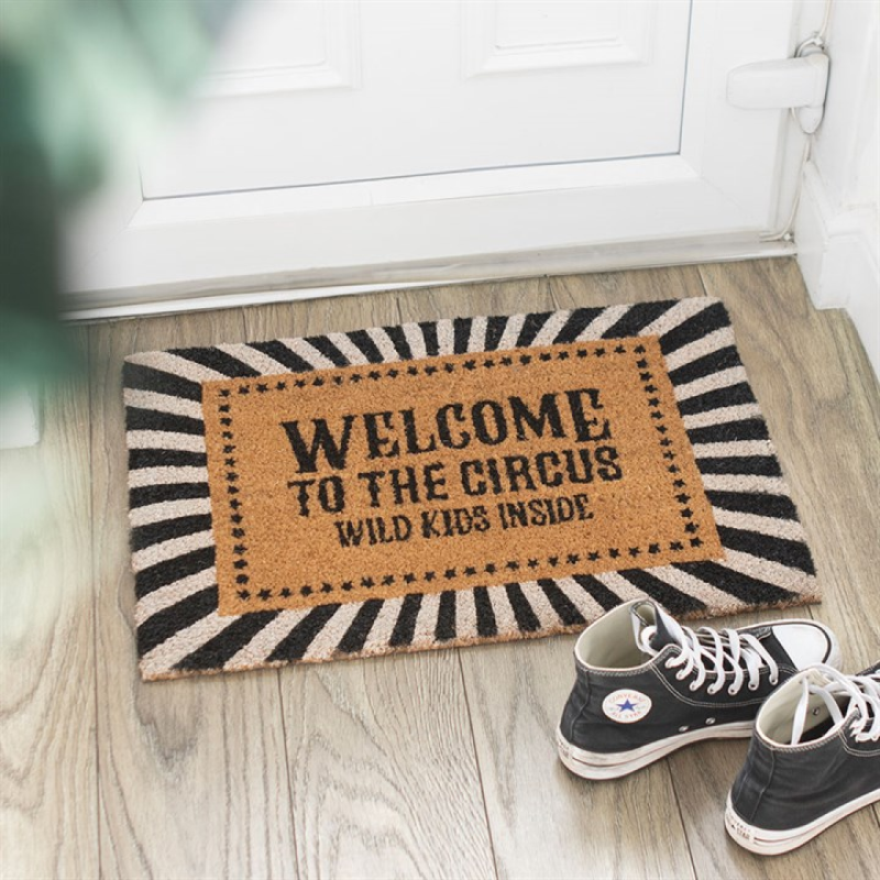 Doormat with 'Welcome to the Circus, Wild Kids Inside' text on a wooden floor with shoes nearby.