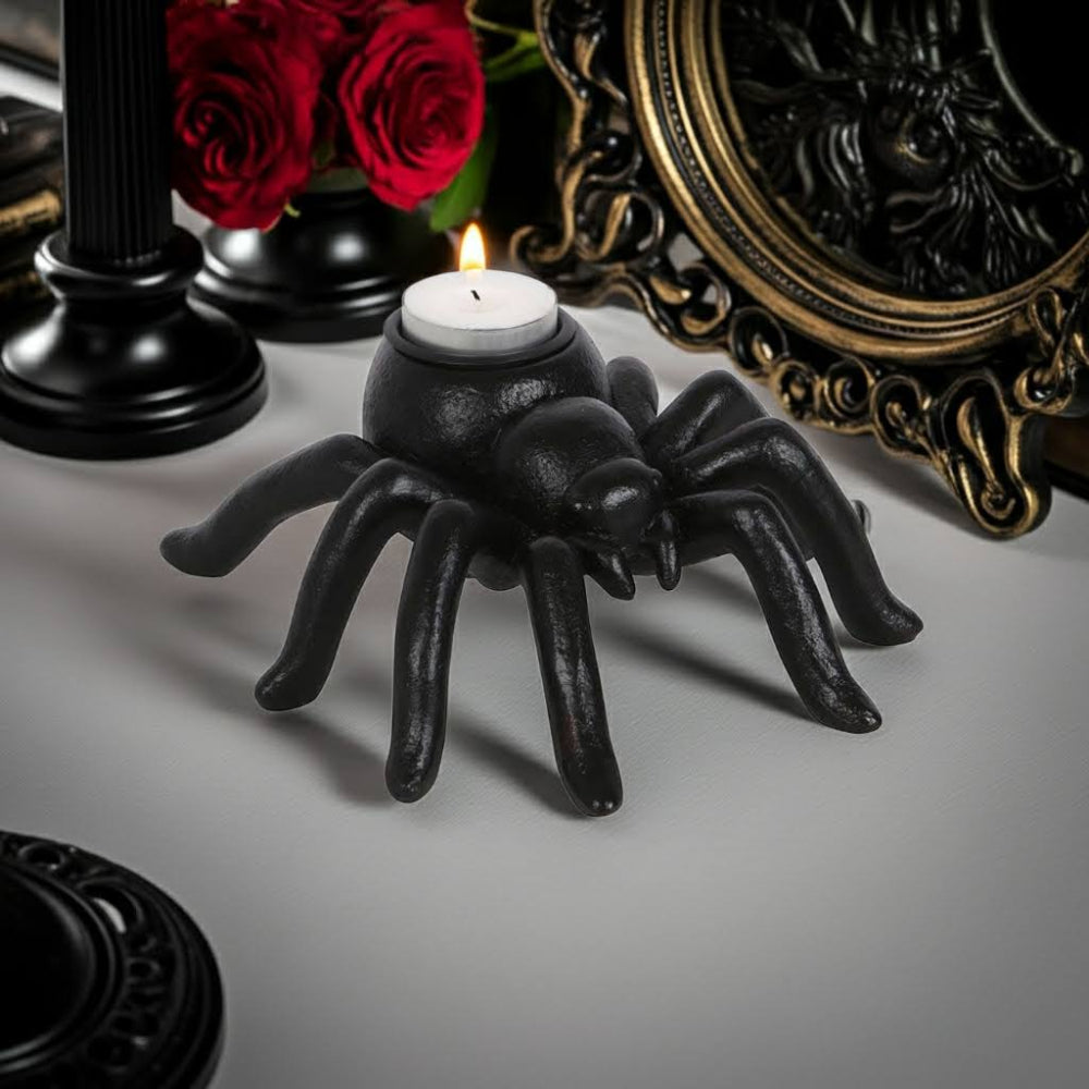 Black spider-shaped candle holder with a lit candle on a gray surface, surrounded by decorative elements.
